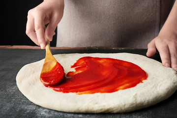 Wall Mural - Female hands making traditional pizza on black table, close up