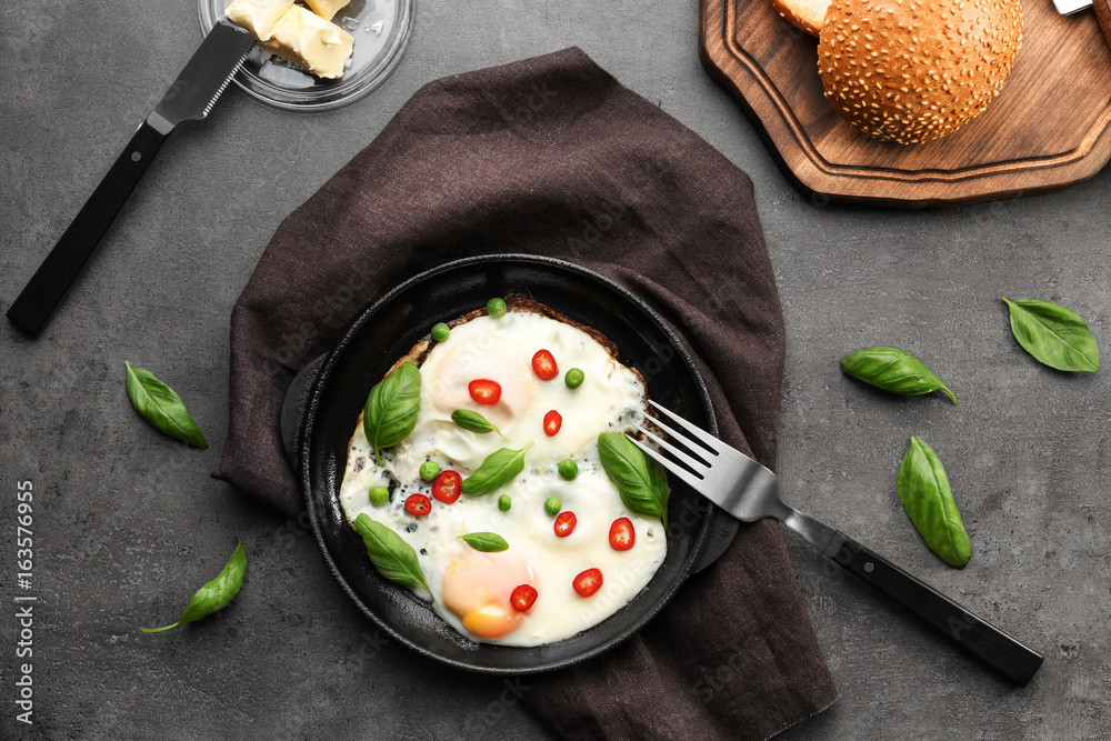 Delicious over hard eggs with green peas, pepper and basil leaves in pan on kitchen table