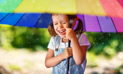 Wall Mural - Happy child girl laughs and plays under summer rain with an umbrella