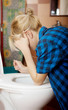 © Piotr Marcinski - Sick young woman leaning on open toilet seat.