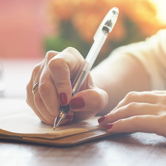 woman's hand with red nails writing some message note or letter to notebook by pen