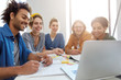 © wayhome.studio  - Group of five mixed race students sitting together surrounded with books looking happily at laptop making video call to their friend abroad being glad to see him. University friends with books, laptop