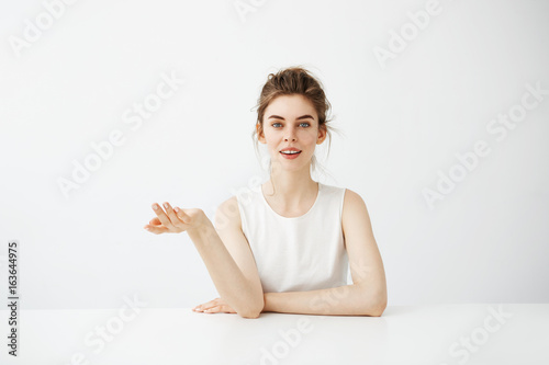 Fotografie, Obraz Dreamy beautiful young girl with bun sitting at table over white background thinking dreaming looking at camera