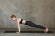 Young woman practicing Plank, Dandasana yoga pose against texturized wall / urban background