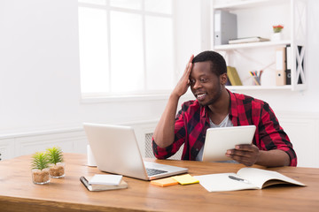 Wall Mural - Black businessman in casual office, work both on laptop and tablet