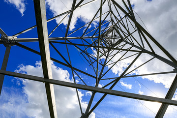 The electricity transmission pylon in daytime outdoors. Electricity tower standard overhead power line transmission tower on the background blue sky and white cloud. 