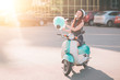 © estradaanton - Young happy hipster woman eating sweetened cotton candy. Female model riding a blue scooter a city street