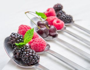 Wall Mural - Fresh berries on steel spoons on white marble background