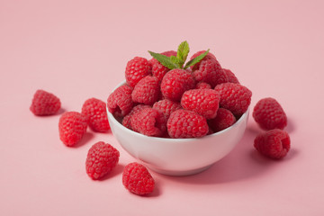 Bowl with fresh raspberries and mint leaves on a pink background. Minimal concept