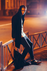 Young scary handsome casual student in hood outdoors. Portrait of hooded guy walking through night city