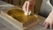 Close up hands of carpenter woodworker rubs lacquer on a wooden plank