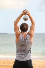 Wall Mural - Fitness exercise with dumbbells - Man doing Standing Dumbbell Triceps overhead Extension exercises. Fit male fitness model workout outside on beach gym.