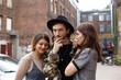 © shurkin_son - Love triangle between man and two women. Outdoor shot of bearded hipster in trendy hat looking at camera with thoughtful expression, choosing between beautiful females who standing next to him
