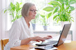 © agenturfotografin - Senior woman at home with a calculator and lots of receipts in front of her laptop making her annual tax declaration