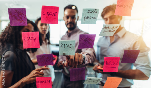 Fotografía Business team looking at sticky notes posted on glass wall in o