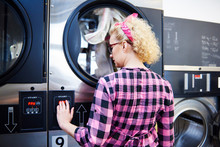 Woman Pressing Washing Machine Buttons At Laundrette