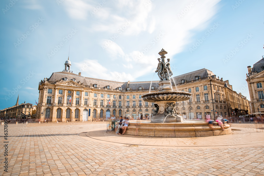 View on the famous La Bourse square with fountain in Bordeaux city, France. Long exposure image technic with motion blurred people and clouds - obrazy, fototapety, plakaty 