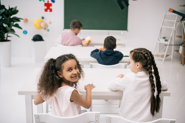 Wall Mural - Back view of cute multiethnic kids sitting at school desks and studing in classroom