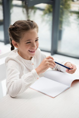 Wall Mural - Cute smiling schoolgirl holding pen and looking away in classroom
