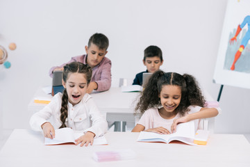 Wall Mural - Cute smiling multiethnic pupils studying with textbooks in classroom