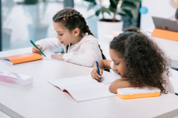 Wall Mural - Adorable multiethnic schoolgirls writing and studying at desk in class