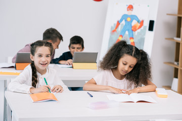 Wall Mural - Multiethnic group of pupils writing in exercise books and using digital tablets during lesson