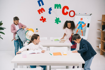 Wall Mural - Multiethnic group of schoolchildren preparing for lesson in classroom