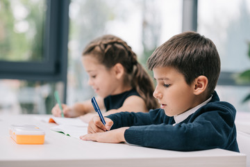 Wall Mural - Close-up portrait of classmates sitting at desk and writing in exercise books