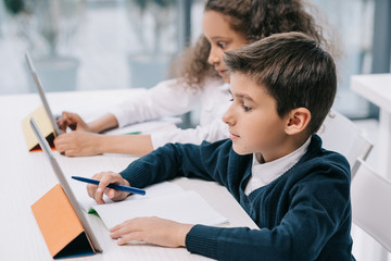 Wall Mural - Cute focused multiethnic schoolchildren using digital tablets while studying in classroom