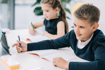 Wall Mural - Schoolchildren writing in blank exercise books while studying at desk in classroom