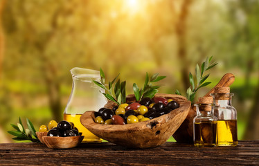 Freshly harvested olives berries in wood bowls and pressed oil in glass bottles