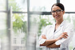 Beautiful young scientist in eyeglasses standing with crossed arms and smiling at camera