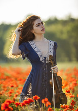 Beautiful Romantic Girl With Red Hair And Blue Dress Holding Violin On Nature Field Of Poppy Flowers. Photo Of Sensual Woman.