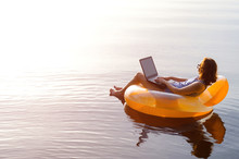 Business Woman Working On A Laptop In An Inflatable Ring In The Water, A Copy Of The Free Space. Workaholic, Work On Vacation.