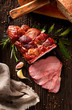 © zi3000 - Smoked ham sliced on a wooden rustic table with addition of fresh aromatic herbs, top view.