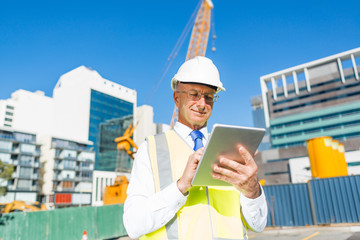 Construction manager controlling building site and tablet device in his hands