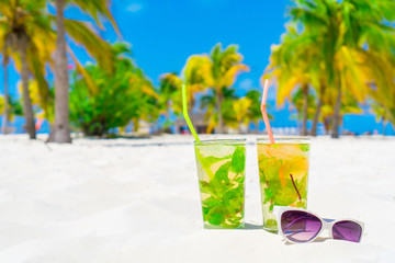 Wall Mural - Two cold tasty mohito cocktails and white sunglasses on the white sandy beach