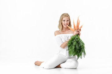 Canvas Print - Beautiful blond woman  holding fresh carrot with green leaves on white background. Health and Diet