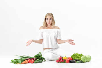 Sticker - Frustrated blond woman spreads hands in both directions and lots of fresh vegetables on white background