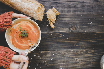 Hands holding hot cream soup on the wooden table, top view. With copy space