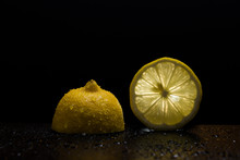 A Slice Of Lemon And Half Of Lemon With Back Light On A Black Background With Water Drops