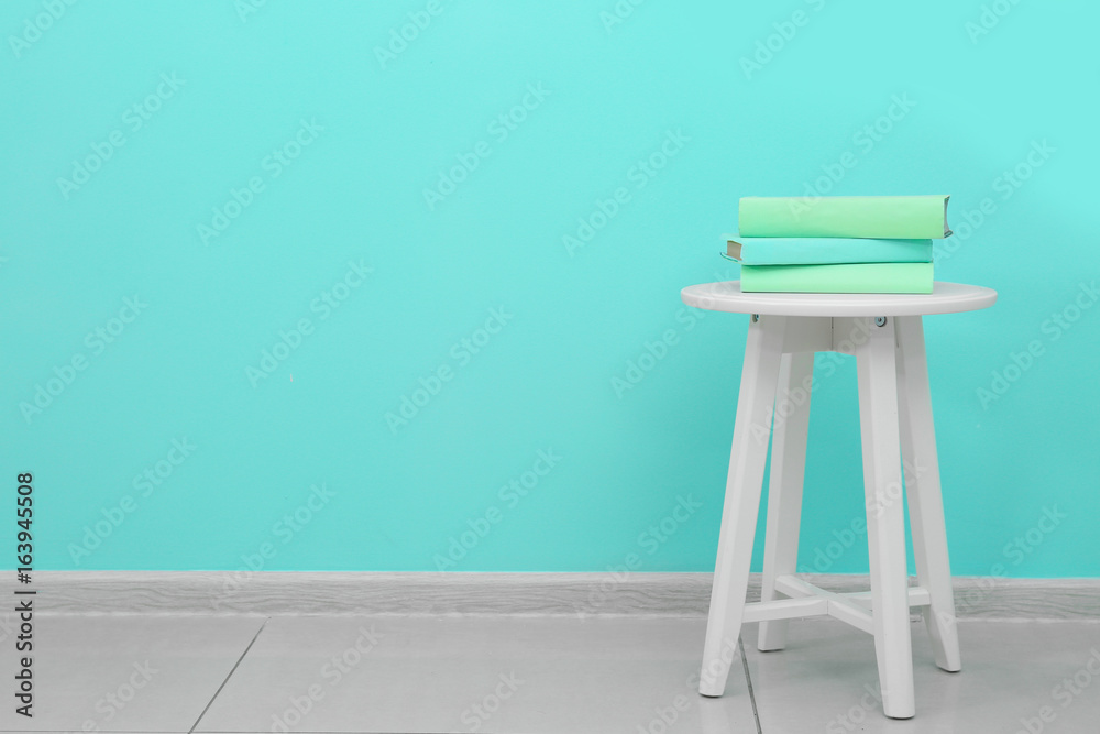 Trendy stool and books near mint wall indoors