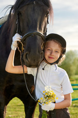 Pretty little girl jockey communicating with her black horse in professional outfit