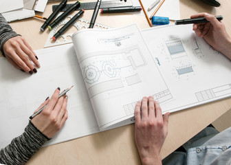 Wall Mural - Designers hands drawing scheme of piece of furniture on creative desk top view. Unrecognizable man and woman working together in architecture workplace