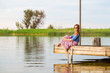 © Kirill Gorlov - Beautiful young red woman sitting on a wooden pier in a colorful long sarafan dress and putting her leg in a water