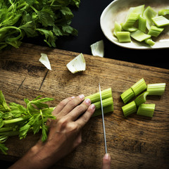 Wall Mural - Aerial view of hands with knife cutting celery on wooden cut board