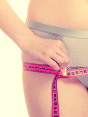 Woman in lingerie measuring her hips with measure tape.