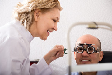 Mature blonde woman ophthalmologist and  smiling man pensioner check eyesight in clinic