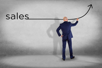 Businessman in front of a wall writing the word sales with a arrow - business concept