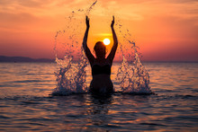 Silhouette Of Female Splashing Water With Her Hands At Sunset Over Sea